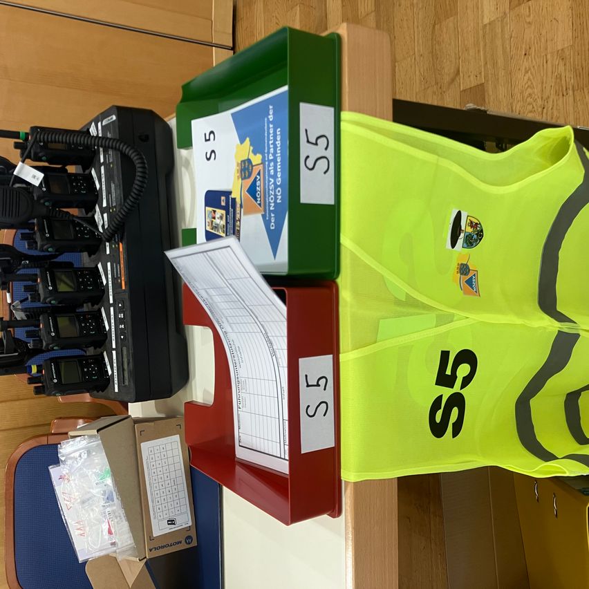 A fluorescent vest with the number 55, along with a red and green storage box, a document, and a black device with a cord.