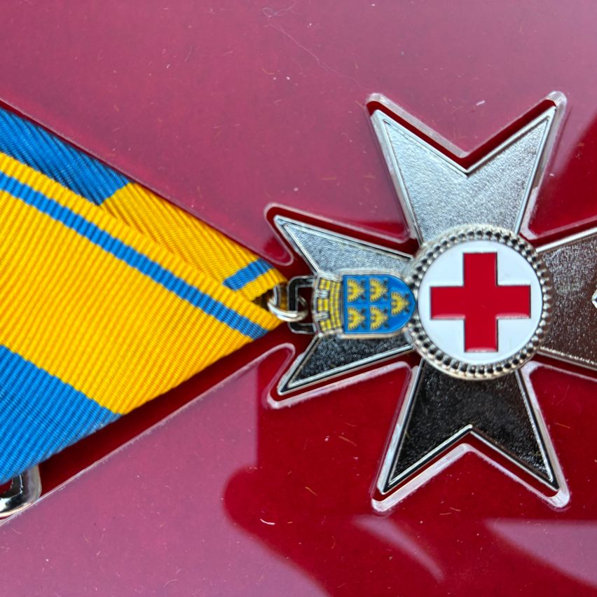 Ein Nahaufnahme eines roten Kreuz-Ordens mit einem blau-gelben Band, das an einem roten Hintergrund befestigt ist.