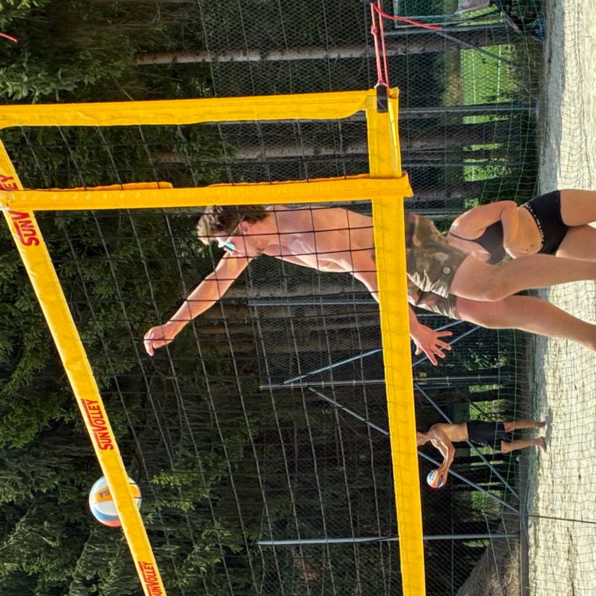 Ein Mann taucht, um einen Volleyball über ein Netz zu schlagen, während ein anderer Mann nach dem Ball greift.