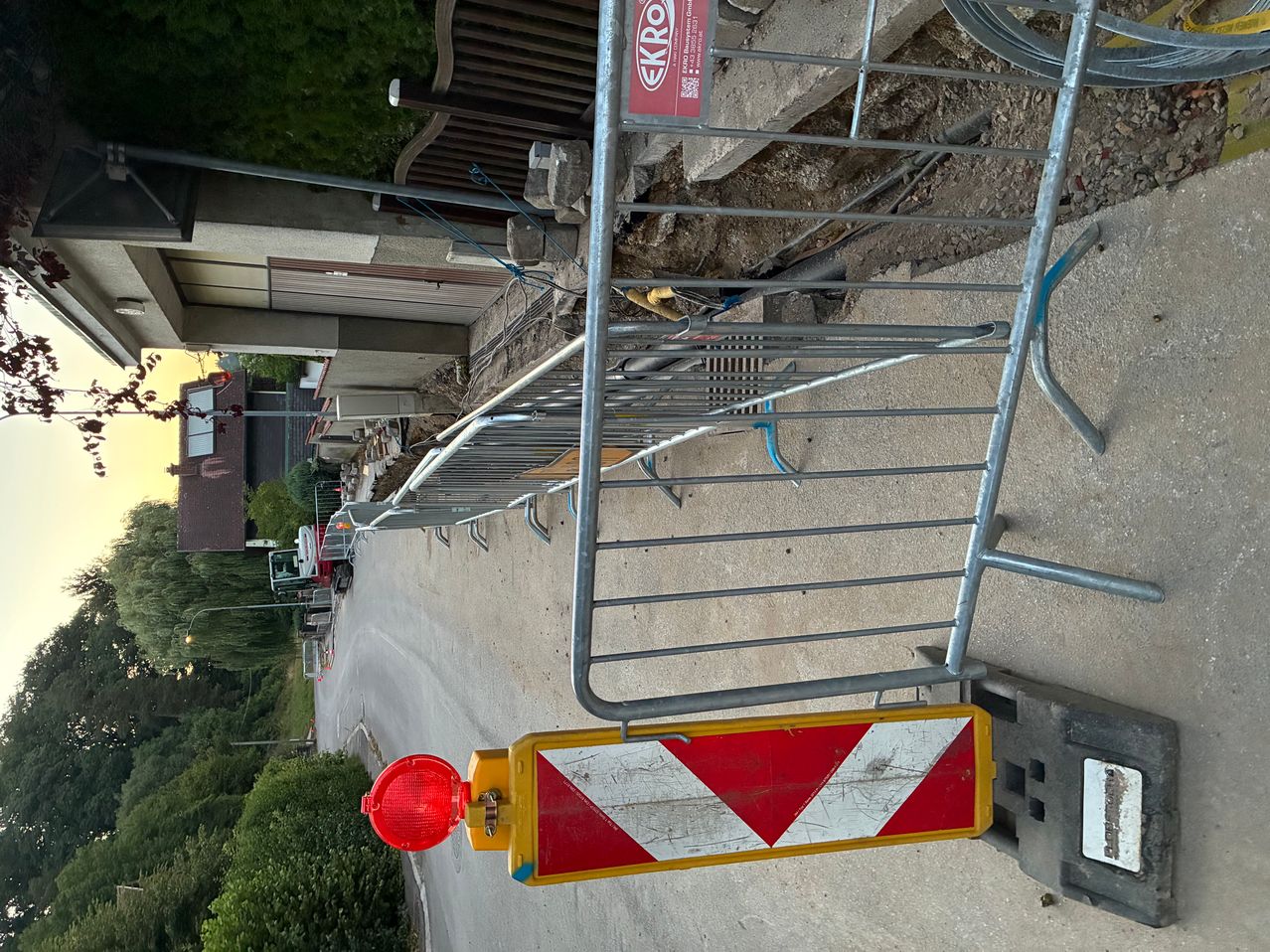 Baustelle mit Absperrgitter und Warnleuchte in einer Wohnstraße, Bagger im Hintergrund