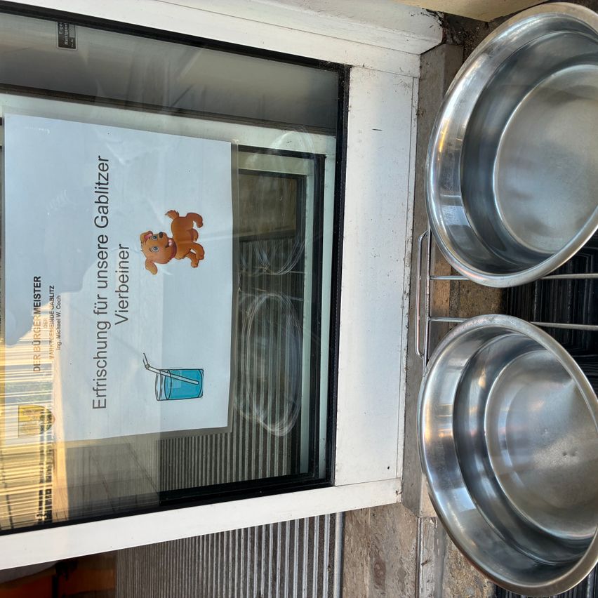 Ein Glasfenster mit einem Schild auf Deutsch und zwei Edelstahlschüsseln an der Seite.