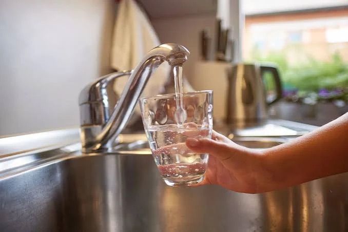 Eine Person füllt ein klares Glas mit Wasser aus einem Küchenhahn.