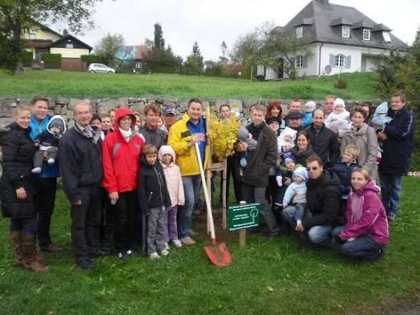 Baumpflanzaktion mit vielen Personen in einem Garten vor einem Haus