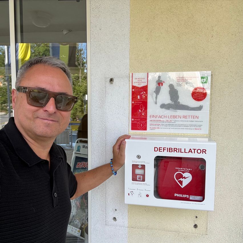 Mann mit Sonnenbrille neben Defibrillator-Kasten an Hauswand in Österreich