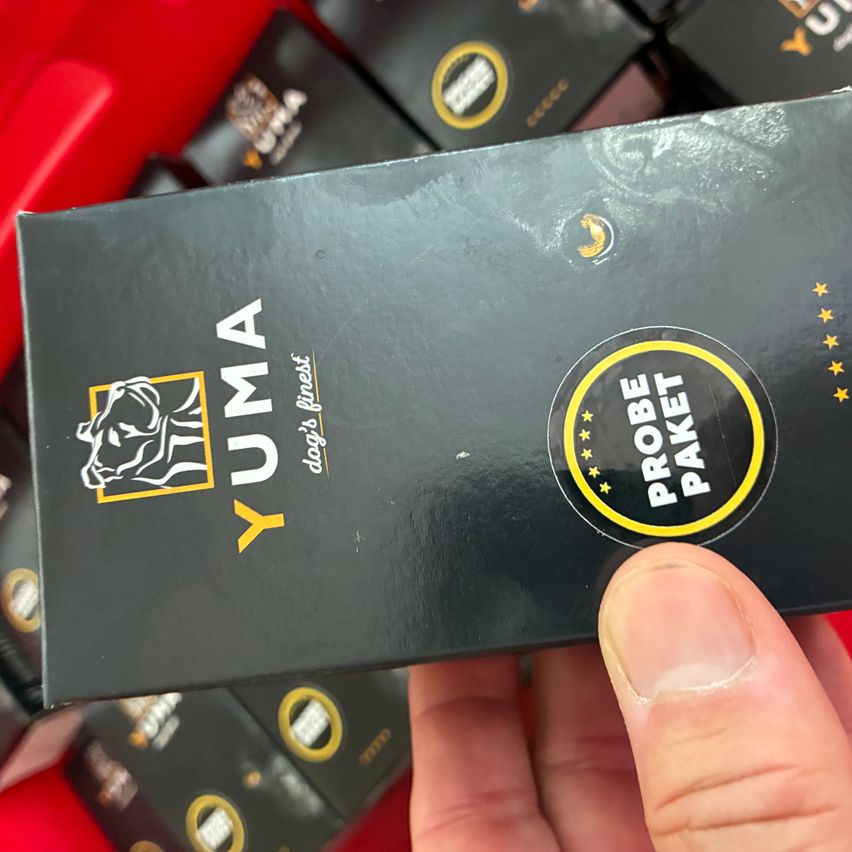 A person holds a black box labeled YUMA with a yellow logo and text PROBE PAKET in a store.