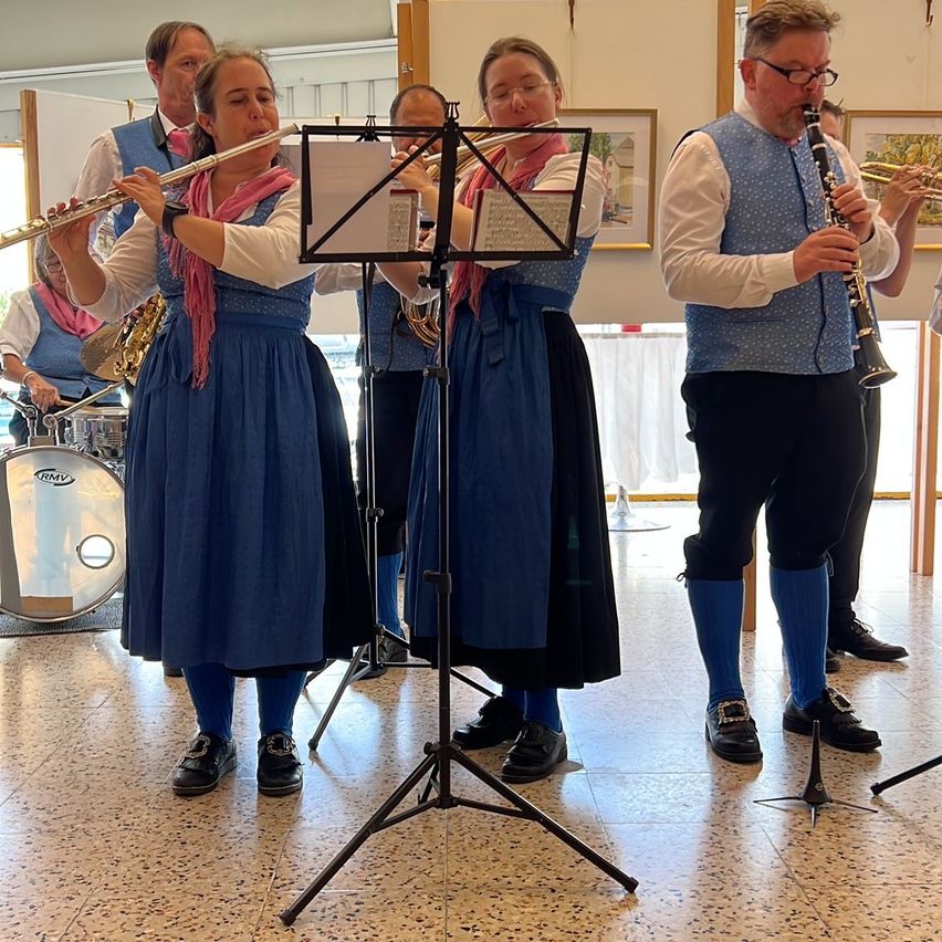 Eine Gruppe Musiker in traditioneller blauer Kleidung spielt verschiedene Instrumente, darunter Flöten, Klarinetten und eine Trommel, in einer Aufführungsumgebung.