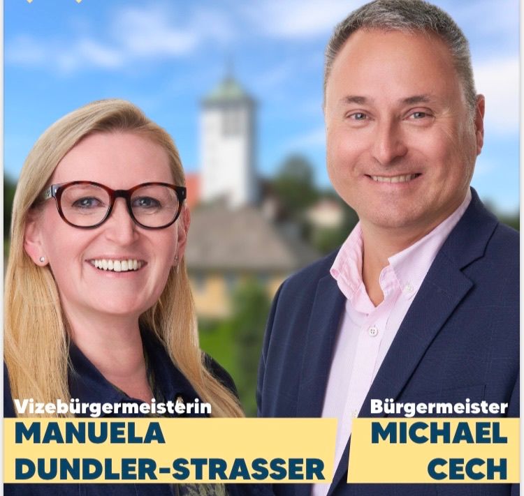 Ein lächelnder Mann und eine Frau stehen lächelnd vor einem blauen Himmel. Die Frau trägt eine Brille und ein blaues Oberteil, und der Mann trägt einen Anzug. Unten steht der Text 'Vizebürgermeisterin Manuela Dudler-Strasser' und 'Bürgermeister Michael Cech'.