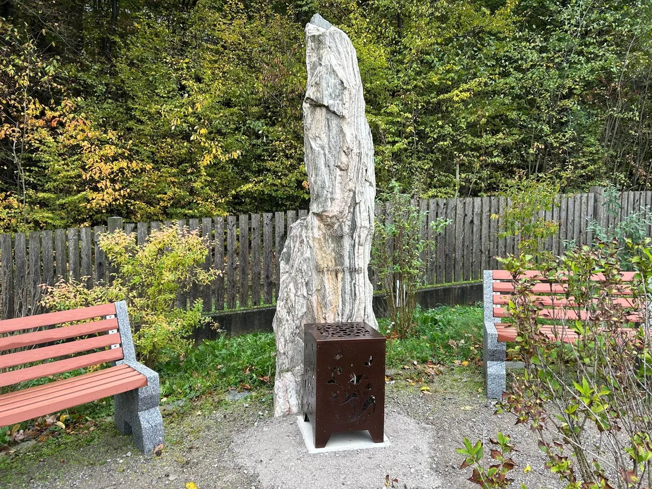 Gedenkstätte mit Stein und Feuerstelle in einem Garten mit Bänken