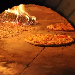 Ein Pizzaofen mit zwei Pizzen darin. Eine Pizza hat geschmolzenen Käse und die andere hat eine verbrannte Kruste.