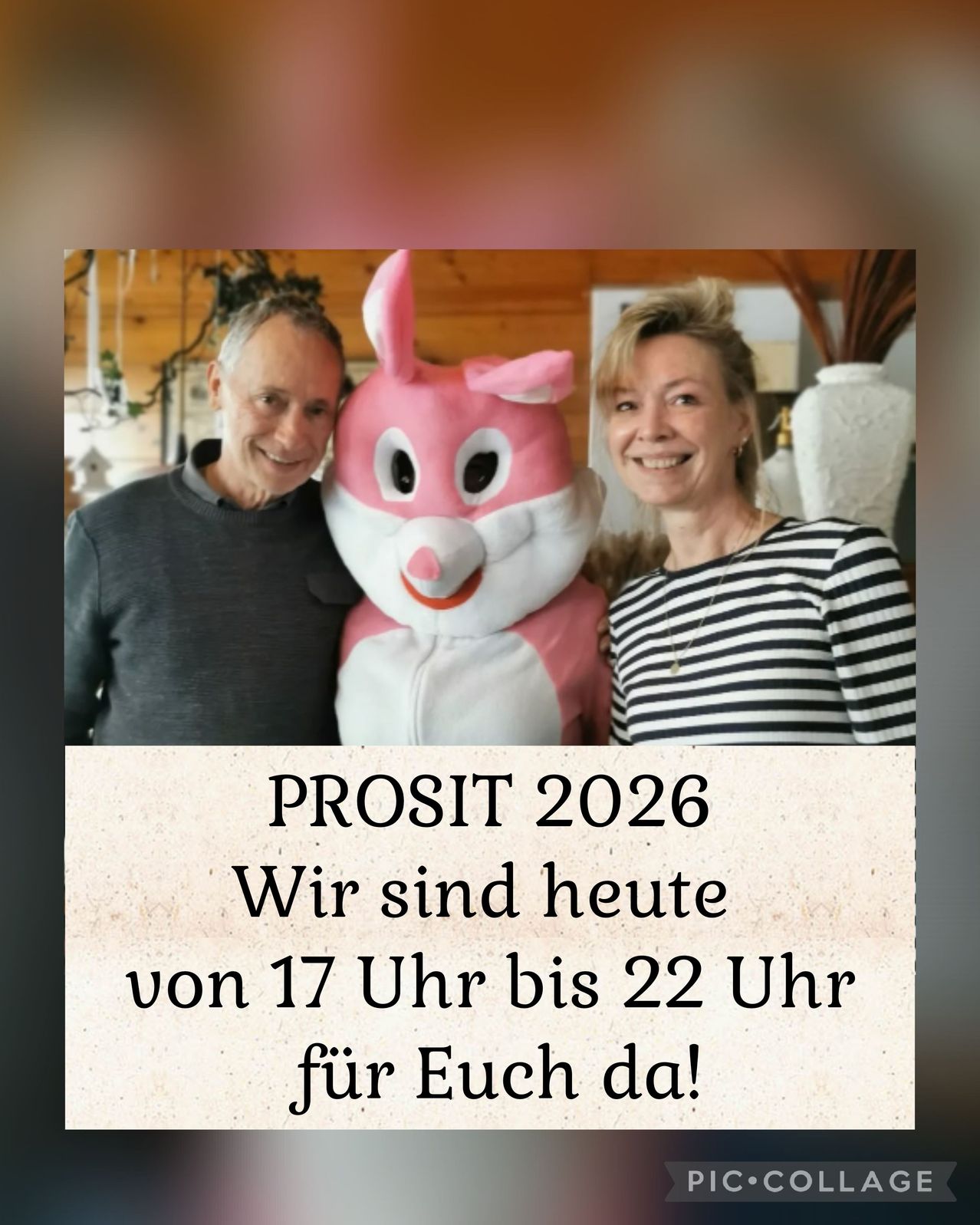 Ein Mann und eine Frau stehen mit einem rosa Maskottchen in einem Raum. Der Text lautet 'PROSIT 2026 Wir sind heute von 17 Uhr bis 22 Uhr für Euch da!'.
