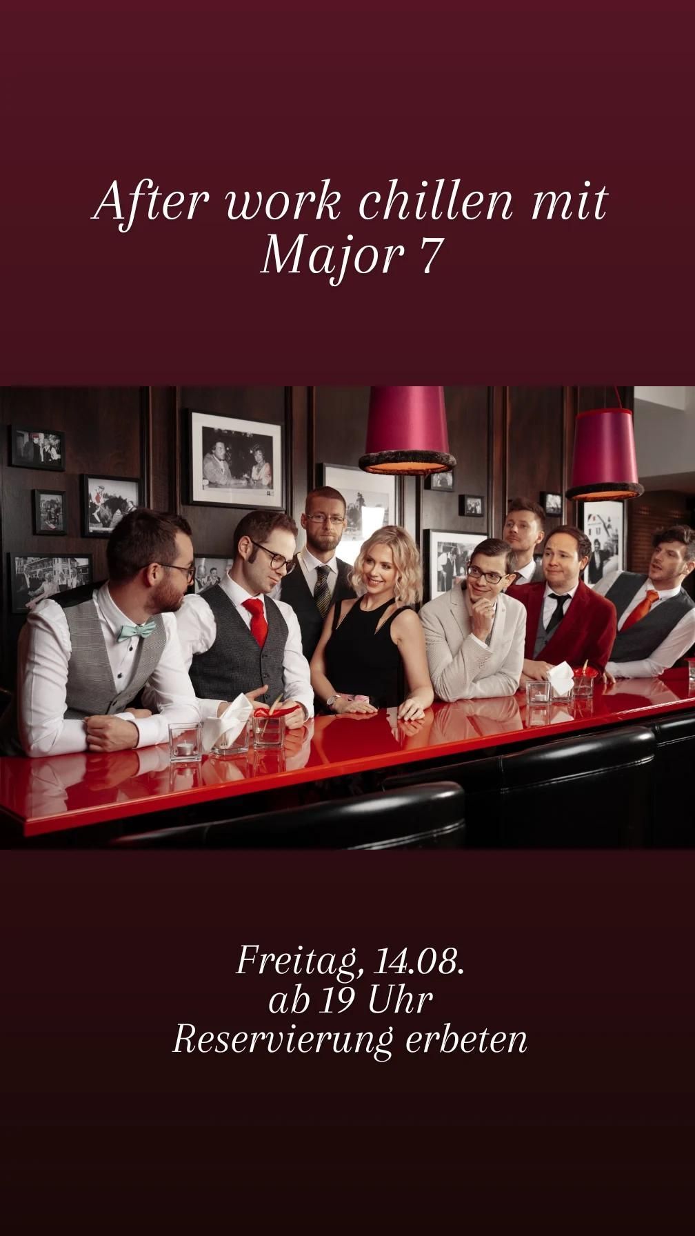 Eine Gruppe von Menschen in formeller Kleidung sitzt an einer Bartheke, lächelt und posiert für ein Foto. Die Bartheke hat eine rote Oberfläche und ist mit Gläsern und Servietten geschmückt. Die Wand hinter ihnen ist mit Bilderrahmen dekoriert.