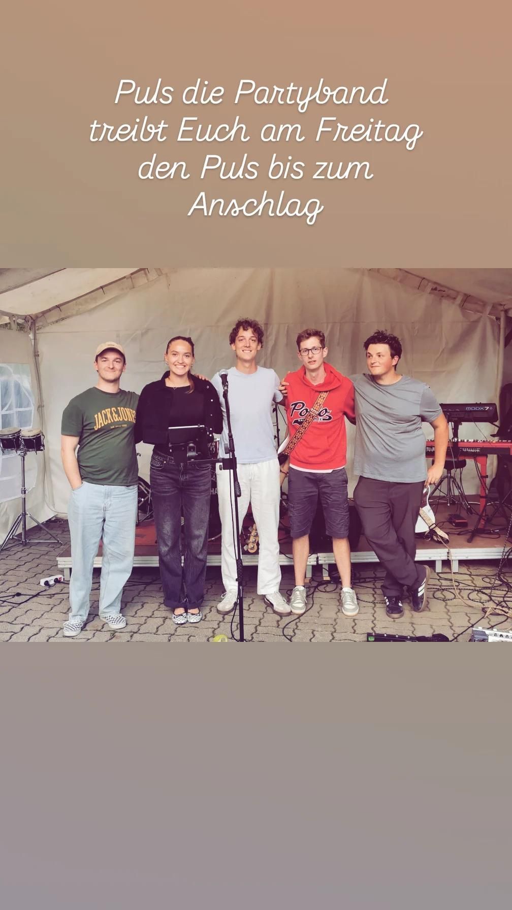 Fünf Personen stehen vor einem Zelt. Ein Mann hält ein Mikrofon, und ein anderer Mann hat eine Gitarre. Hinter ihnen befinden sich Musikinstrumente wie Trommeln und Keyboards.