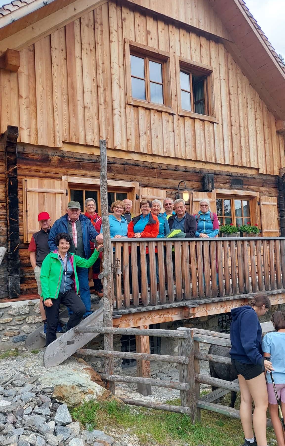 Eine Gruppe von Menschen steht auf der Veranda eines Holzhauses, lächelt und posiert für ein Foto.