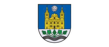 Das Wappen zeigt eine Kirche mit zwei Türmen, einem Kreuz obenauf und einem Löwen, alles vor einem blauen Hintergrund, mit grünen Blättern und Trauben darunter auf einer welligen weißen Linie.