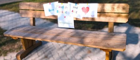 A wooden bench with signs reading 'Plauder-Bankerl', 'Aile sind', '-lich', and 'willkommen!'. The bench is in a park. At the bottom, logos for 'Gesundheit Osterreich GmbH' and 'Fonds Gesundes Osterreich' appear.