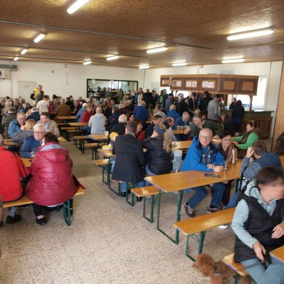 Ein überfüllter Indoor-Essbereich mit vielen Menschen, die an Tischen sitzen, einige mit Getränken und Essen, einige stehen und ein Hund unter einem Tisch.