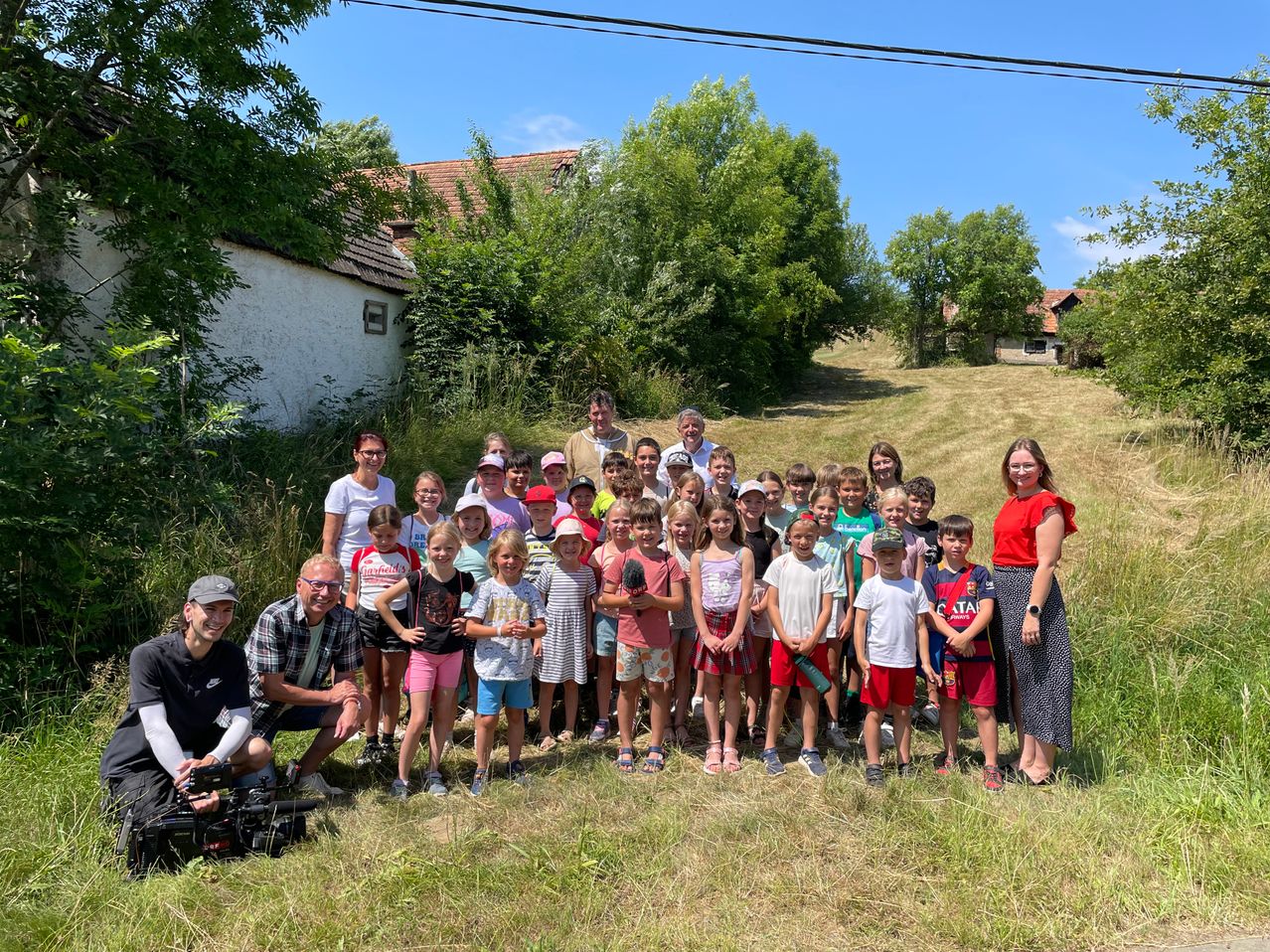 Eine Gruppe von Kindern und Erwachsenen posiert für ein Foto auf einer Rasenfläche, mit einem Haus und Bäumen im Hintergrund.