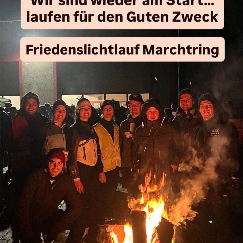 Eine Gruppe von Menschen steht um ein Lagerfeuer herum. Sie sind in warme Winterkleidung gekleidet. Der Text darüber lautet: 'Wir sind wieder am Start... laufen für einen guten Zweck.' Ein weiterer Text lautet: 'Friedenslichtlauf March Tring.' Das Bild hat einen dunklen Hintergrund.