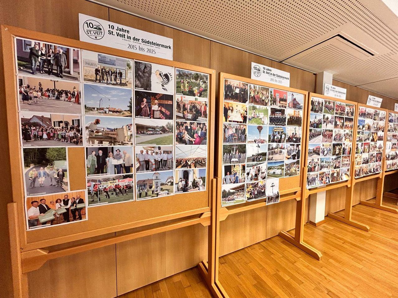 Eine Fotoausstellung zeigt mehrere Fotos, einschließlich Veranstaltungen, Gebäude und Menschen, zur Feier von 10 Jahren St. Veit in Südsteiermark. Die Fotos sind chronologisch von 2015 bis 2025 organisiert.