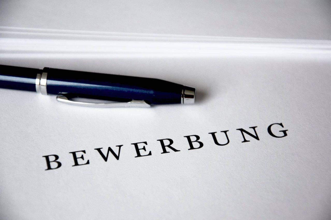A blue pen rests on top of a white paper with the word Bewerbung written on it.