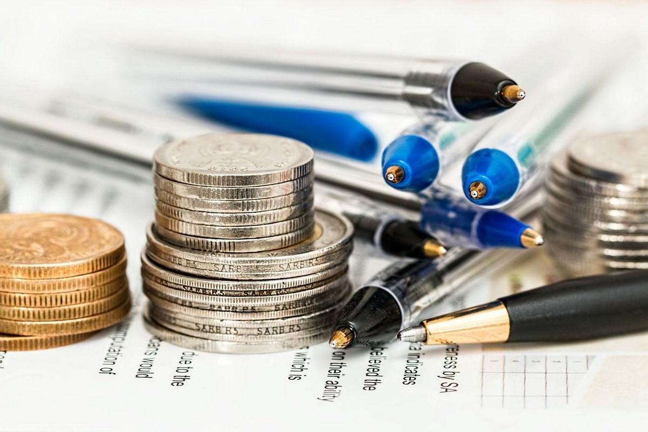 A stack of coins and pens on top of a document. The coins are stacked and some pens are on top.
