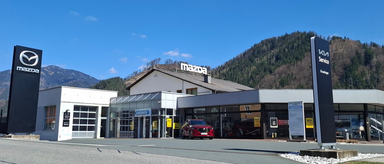 Ein Mazda-Händler mit einem roten Auto davor. Dahinter befindet sich ein Service-Schild und Berge in der Ferne.