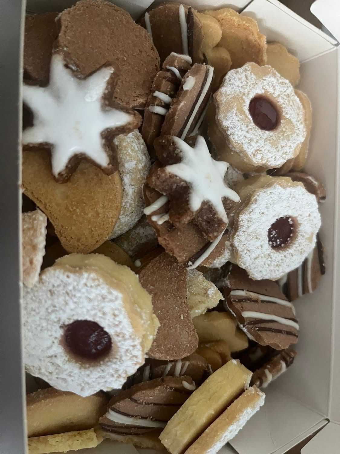 A box filled with an assortment of cookies, including star-shaped, round, and heart-shaped ones, all dusted with powdered sugar.