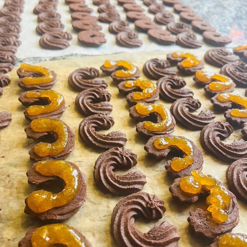A close-up view of chocolate-coated pastries with swirls and orange jam on top, arranged on a parchment-lined surface.