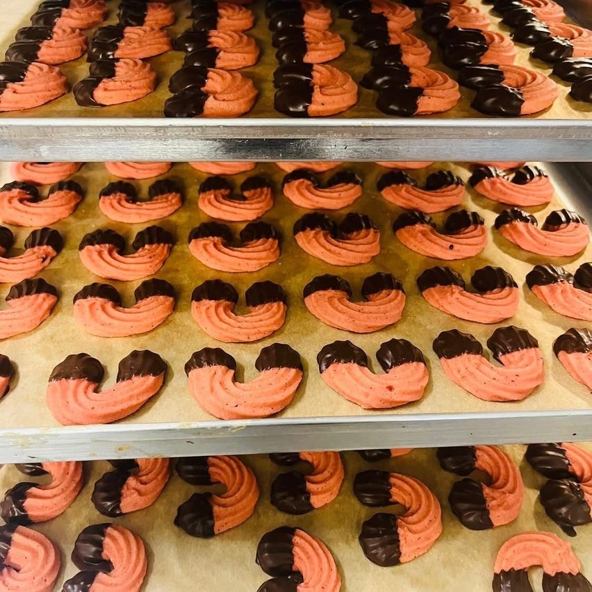 Three trays of pink and black swirl-shaped pastries are arranged in a bakery. The pastries are made with pink frosting and dark chocolate swirls. The trays are stacked on top of each other.
