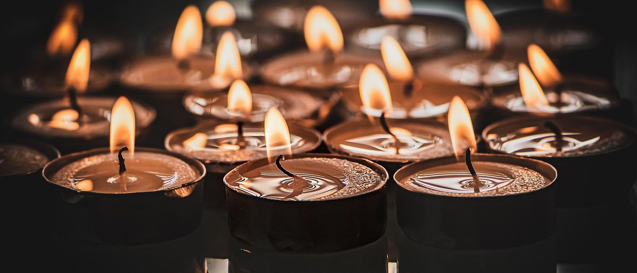 Eine Nahaufnahme von mehreren kleinen Kerzen, deren Flammen in einer dunklen Umgebung brennen.
