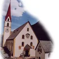 Eine weiße Kirche mit einem roten Turm und einer Uhr befindet sich in einem Berggebiet.