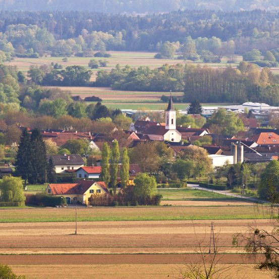 Ein Dorf mit vielen Häusern und einer Kirche, umgeben von grünen Feldern und Bäumen, in einer malerischen ländlichen Landschaft.
