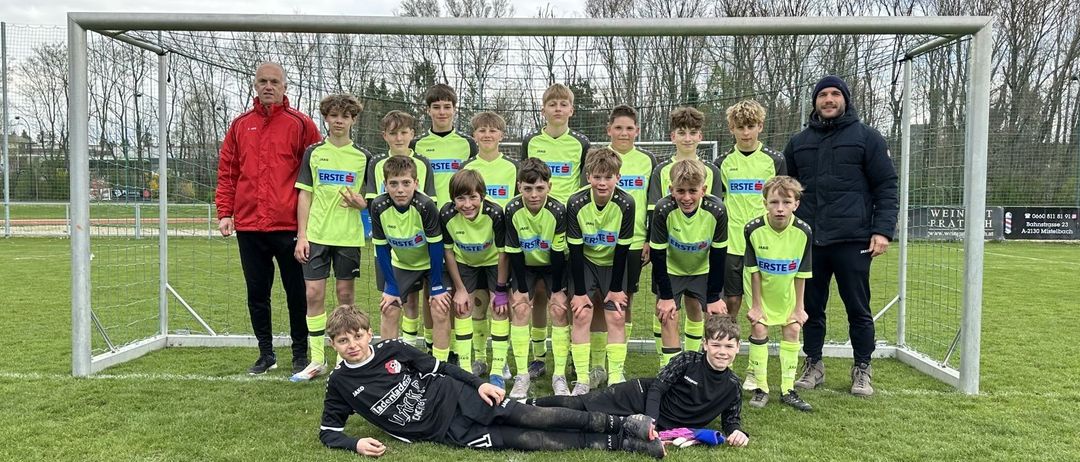Eine Fußballmannschaft mit jungen Spielern in grünen und gelben Trikots posiert für ein Foto auf dem Feld.