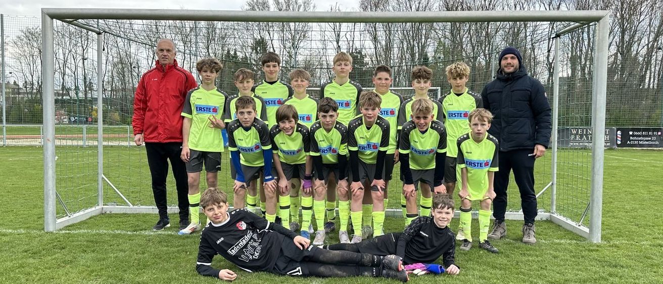 Eine Fußballmannschaft mit jungen Spielern in grünen und gelben Trikots posiert für ein Foto auf dem Feld.