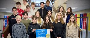 Eine Gruppe von Schülern, die auf einer Treppe stehen und ein blaues Zertifikat für die ICDL-Prüfung halten. Einige tragen Jacken, Brillen und Turnschuhe. Sie posieren für ein Foto.