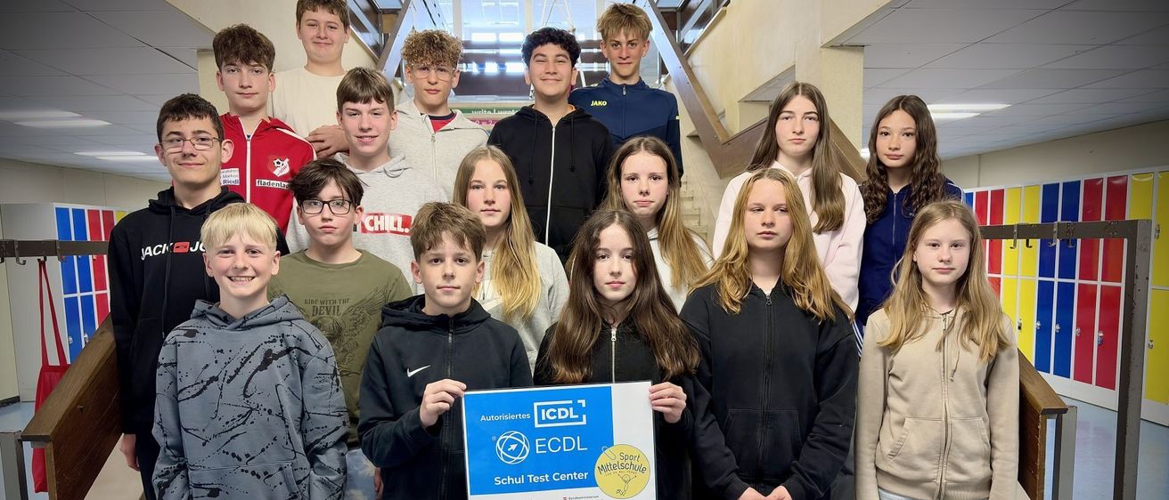 Eine Gruppe von Schülern, die auf einer Treppe stehen und ein blaues Zertifikat für die ICDL-Prüfung halten. Einige tragen Jacken, Brillen und Turnschuhe. Sie posieren für ein Foto.