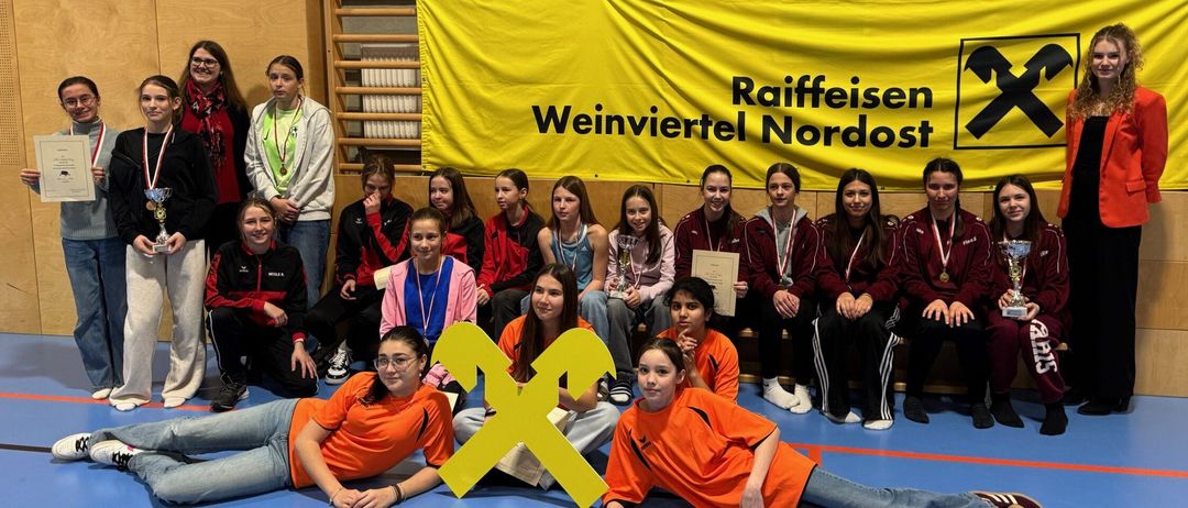 Eine Gruppe junger Menschen in orangefarbenen Uniformen und Medaillen posiert für ein Foto mit einem gelben Banner, auf dem 'Raiffeisen Weinviertel Nordost' steht.