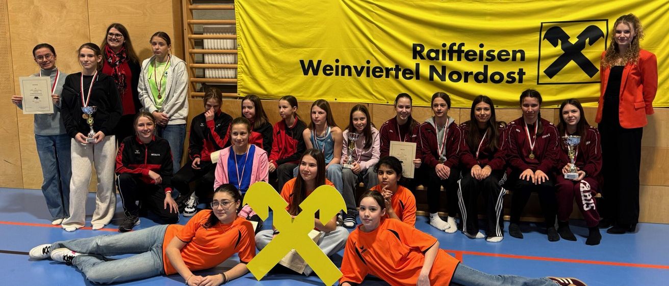 Eine Gruppe junger Menschen in orangefarbenen Uniformen und Medaillen posiert für ein Foto mit einem gelben Banner, auf dem 'Raiffeisen Weinviertel Nordost' steht.