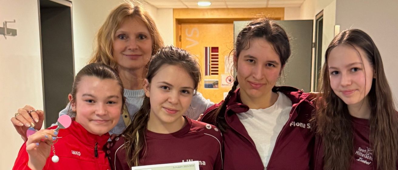 Fünf Mädchen, alle in karmesinroten Jacken, stehen in einem Flur zusammen. Ein Mädchen hält ein Zertifikat für die London Tennis School.