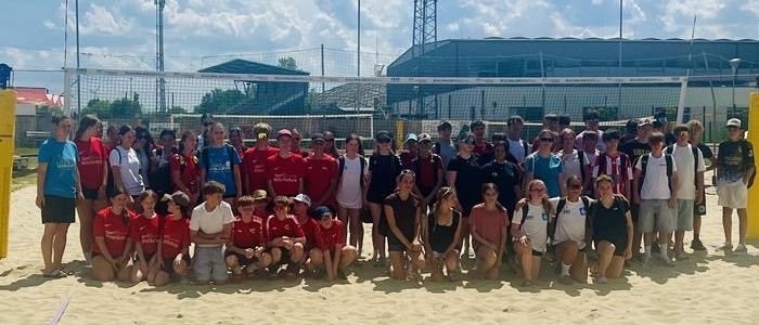 Eine Gruppe von Menschen in roten und weißen Shirts posiert für ein Foto am Strand mit einem Volleyballnetz im Hintergrund.
