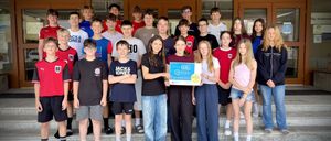 Eine Gruppe junger Leute posiert für ein Foto auf einer Treppe. Sie halten ein blaues Zertifikat mit dem Text ICDL ECDL. Sie tragen Freizeitkleidung und einige haben eine Brille. Hinter ihnen befinden sich Glastüren und Fenster.