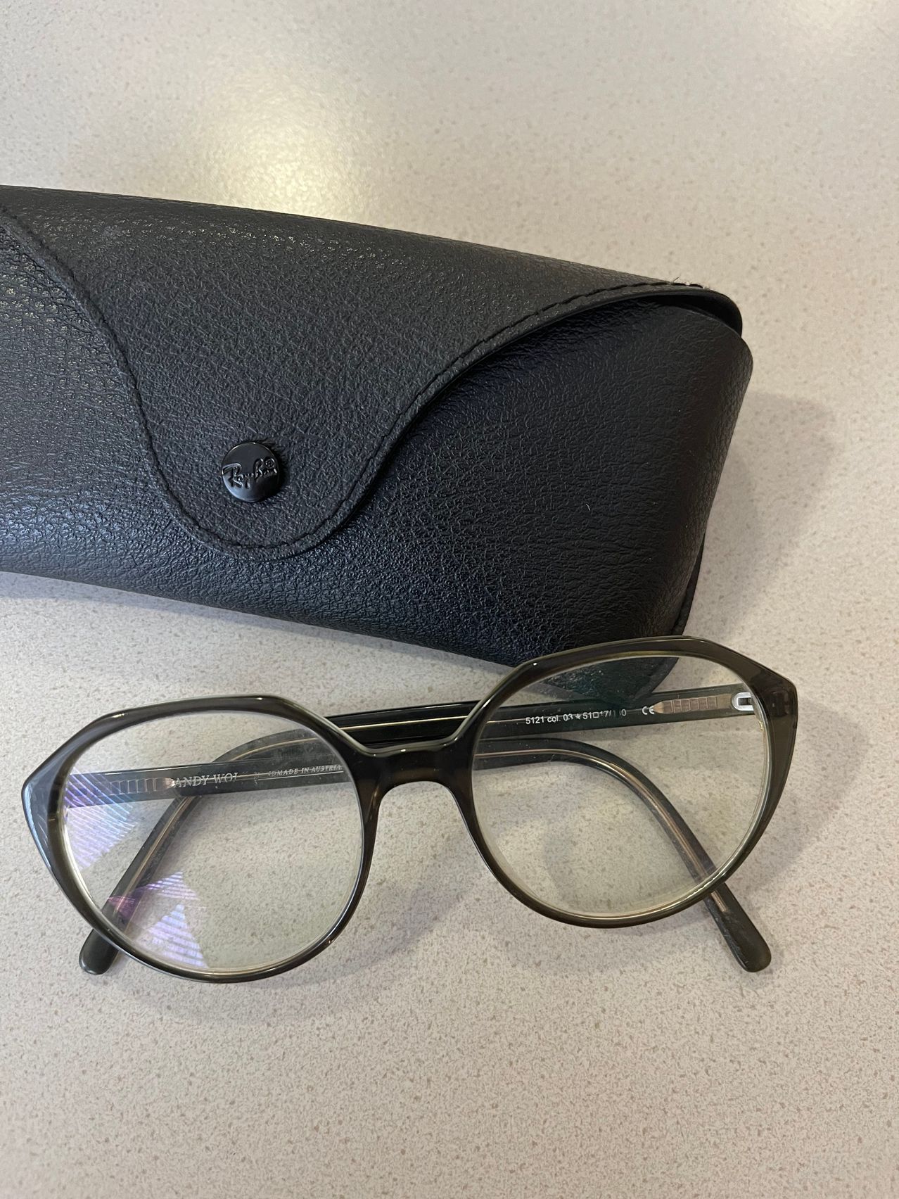 Ein Paar schwarzer Brille mit klaren Gläsern und einem schwarzen Lederetui mit silbernem Logo auf einer weißen Oberfläche.
