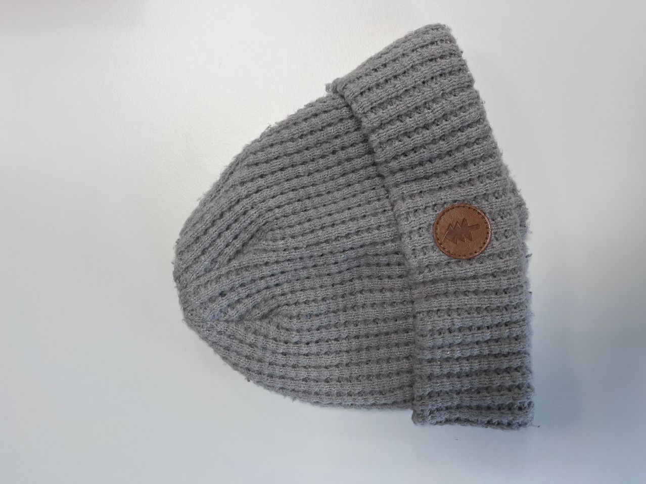 A knitted grey hat with a brown leather patch on the front is displayed against a white background.