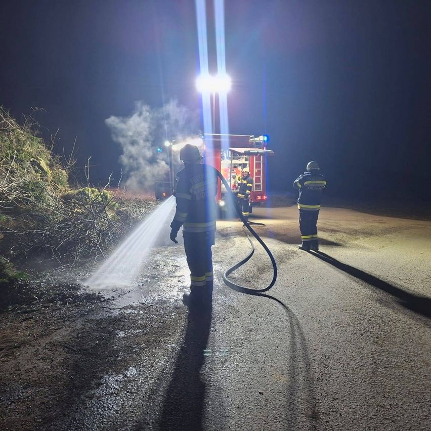 Feuerwehrleute sprühen nachts Wasser auf die Straße. Ein Feuerwehrwagen ist am Straßenrand geparkt.