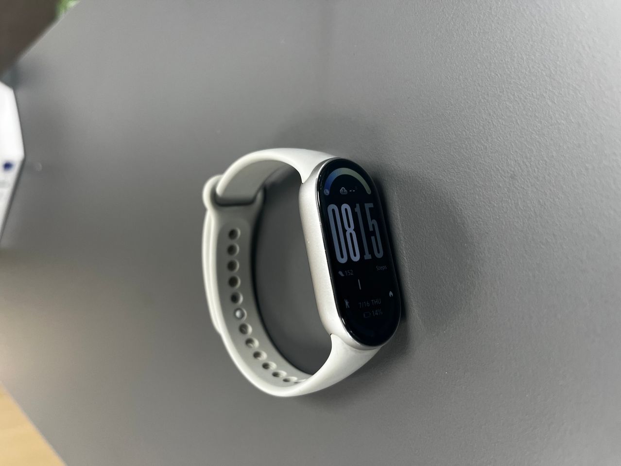 A white fitness tracker with a black face displaying the time 08:15 and additional information such as steps and heart rate.