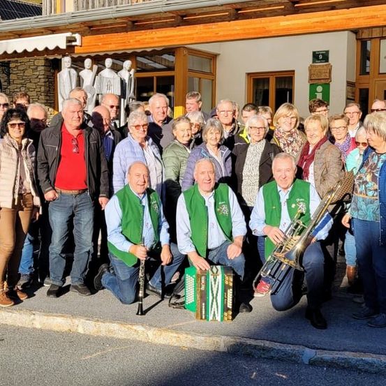 Eine Gruppe von Menschen steht vor einem Gebäude mit Musikinstrumenten. Einige tragen grüne Westen. Sie lächeln für ein Foto.