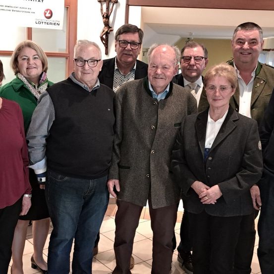 Eine Gruppe von Menschen in formeller Kleidung steht zusammen und lächelt für ein Foto. Sie posieren wahrscheinlich für ein Bild vor einem Schild.