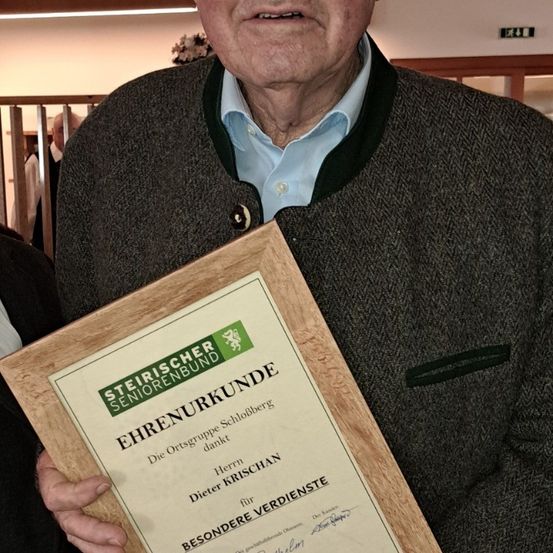 Ein älterer Mann hält ein gerahmtes Zertifikat des Steirischen Seniorenbundes, das Dieter Krischan für besondere Verdienste würdigt.