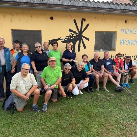 Eine Gruppe von Männern und Frauen posiert für ein Foto vor einem Gebäude mit einem Windmühlendesign an der Wand.
