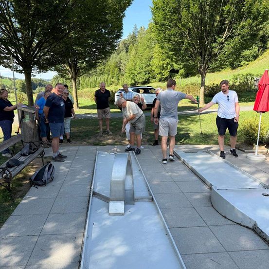 Eine Gruppe von Menschen spielt Minigolf an einem sonnigen Tag, wobei ein Mann kurz davor steht, den Ball zu schlagen.